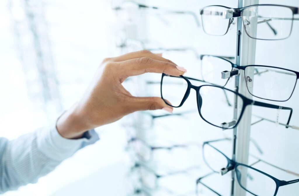 A person selects a pair of eyeglass frames from a display rack filled with various styles of glasses.