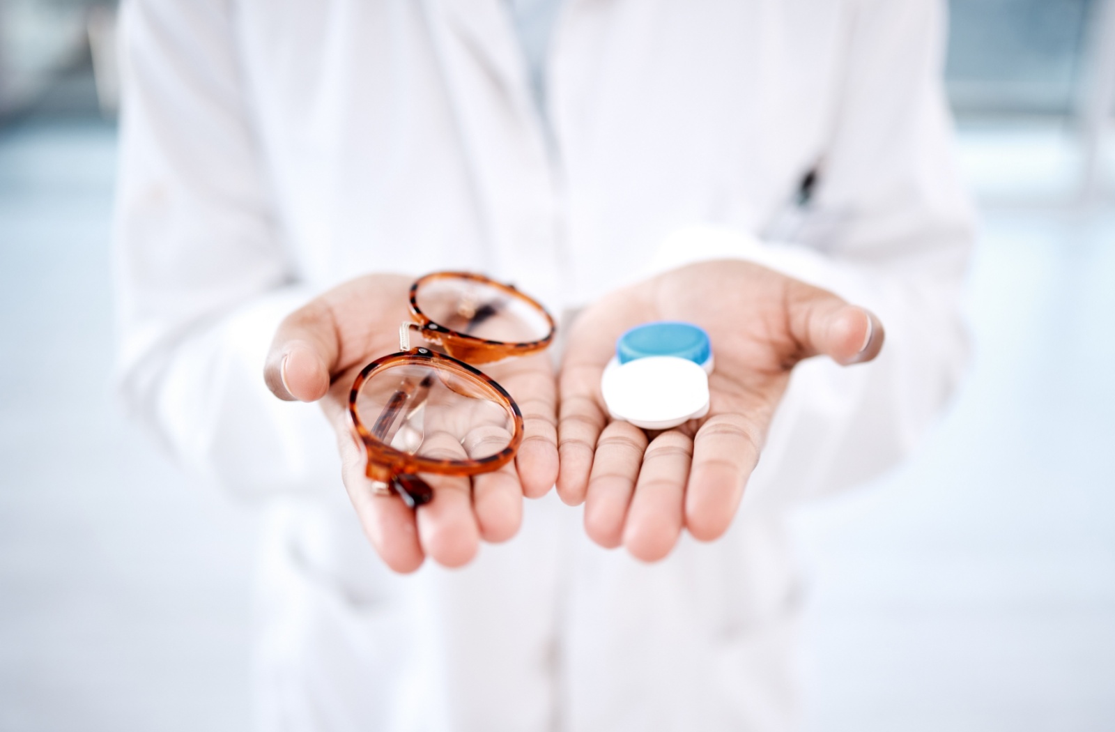 Close up of person holding glasses in one hand and contact lenses in the other.