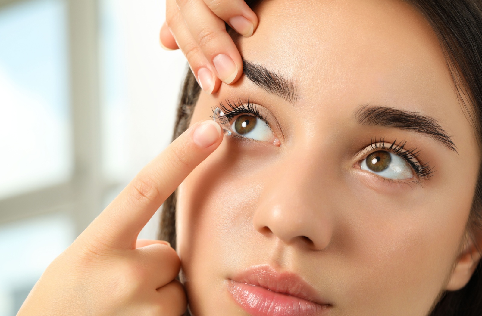 Close up of a person gently pulling their eyelid upwards to put a contact lens in their eye